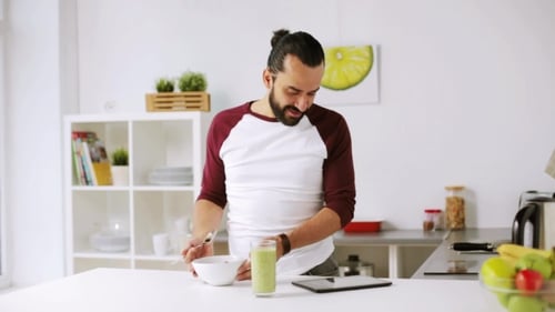 Man Eats Breakfast and Uses Tablet in Kitchen