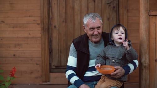 Grandfather Holds Child With Bowl on Cabin Porch