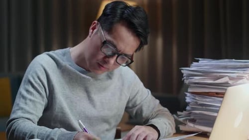 Close Up Of Asian Man Looking At Laptop And Taking Note While Working With Documents At Home
