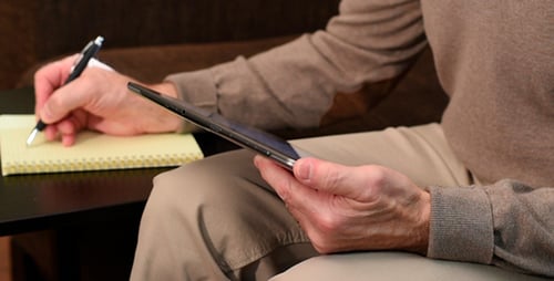 Man Uses Tablet and Writes on Notepad