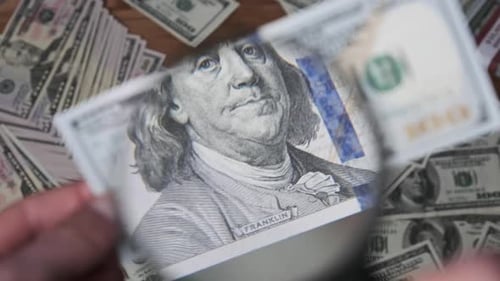 Person Inspects US Currency with Magnifying Glass