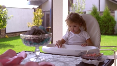 Little Girl Smiles in High Chair Outside Home