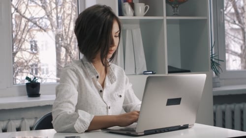 Attractive Business Woman in a White Shirt Works at a Laptop in the Office