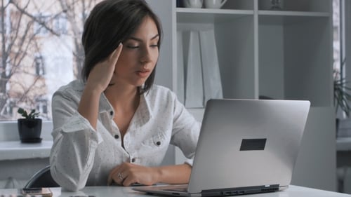 Tired Woman in a Works at a Laptop in the Office
