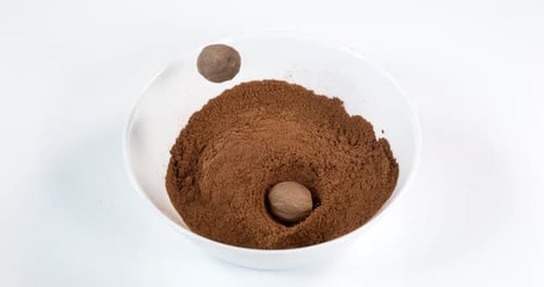 Nutmegs Falling Into Bowl of Brown Powder