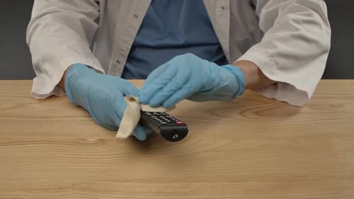 Gloved Hands Sanitize TV Remote with Cloth