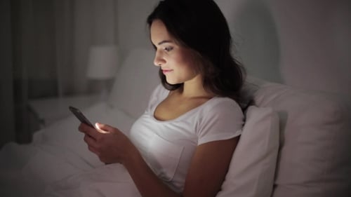 Woman Using Mobile Phone in Bed at Night
