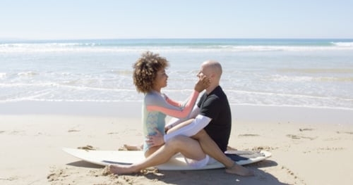 Affectionate Couple Kissing on Surfboard at Beach