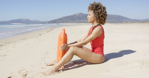 Lifeguard Sitting with Rescue Float on Beach