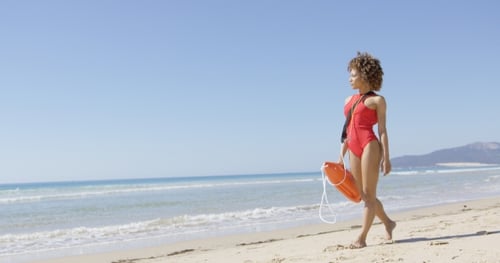 Lifeguard Walks Along Beach with Floatation Device