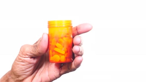 Wrinkled Hand Holding Prescription Pills on White