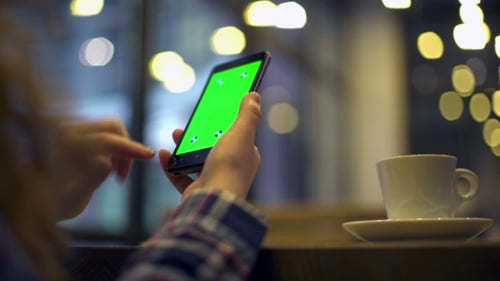 Frau hält Smartphone mit Greenscreen im Café