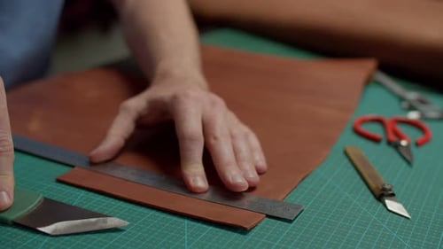 Nahaufnahme eines Lederblatts, das ein Handwerker mit einem Messer im Innenbereich schneidet
