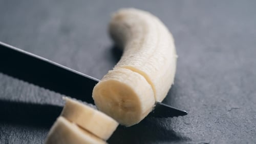 Banana Sliced into Sections with Knife on Gray