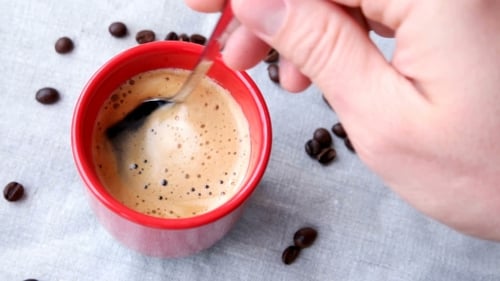 Rote Tasse heißen Kaffees. Mann rührt eine Tasse Espresso ein.