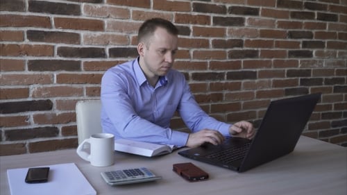 Man Working on Laptop and Writing in Office