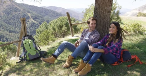 Young Couple Relaxing on Grassy Hillside Hike