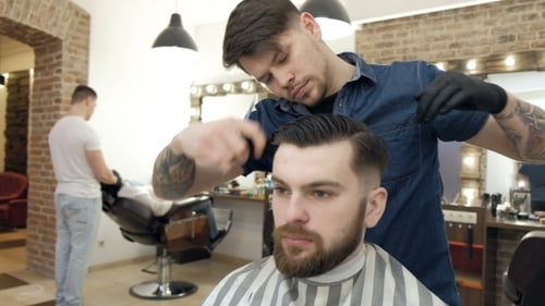 Barber-Stil. Männlicher Friseur im karierten Hemd beim Kämmen der Haare eines männlichen Kunden bei Barbershop