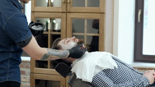Kunde bei der Bartrasur im Friseurladen. Barbier-Tattoo auf seinem Arm