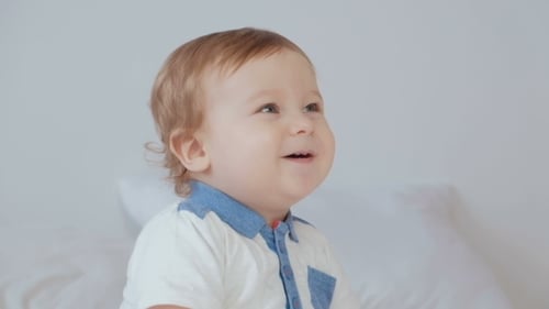 Cute Smiling Baby in a Blue Body Suit on a Beige Couch.