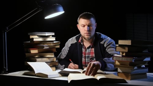 Mann liest ein Buch und schreibt in ein Notizbuch. Schwarzer Hintergrund