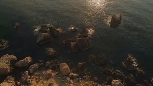 Close up view of rocks in the water on the shore during sunset, with the sunlight shining on the wat