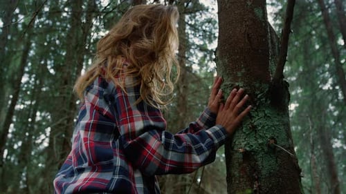 Woman Touching Tree Trunk with Hands in Forest
