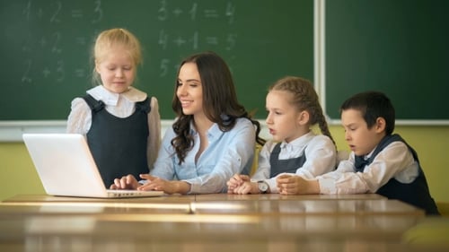 Happy Teacher Using Laptop with Pupils in the Classroom