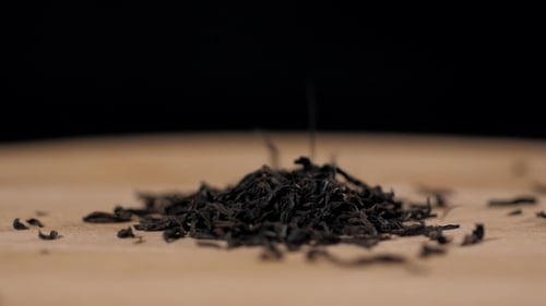 Tea Leaves Being Poured Onto Wood Surface
