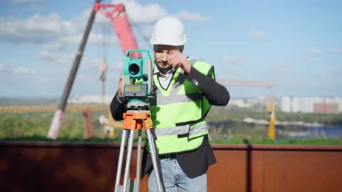 Portrait of Positive Professional Male Engineer Using Theodolite Outdoors Taking Off Hard Hat