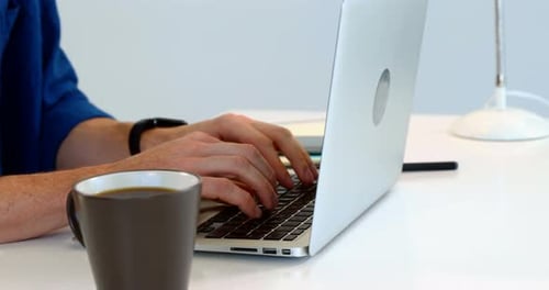 Man having coffee while using laptop on desk against white background