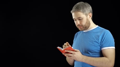 Hübscher Mann im blauen T-Shirt schreibt in seinem roten Notizbuch