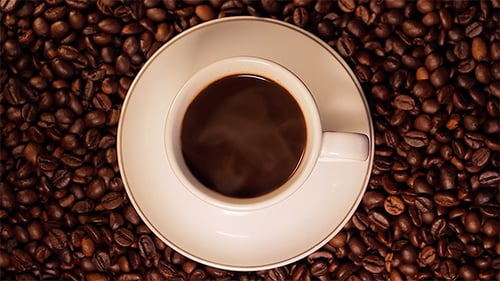 Steaming Coffee Cup Surrounded by Roasted Beans