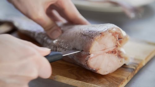 Cutting fresh raw fish with knife on wooden board