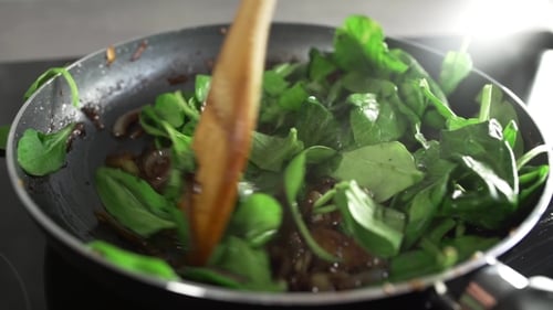 Le cuisinier prépare un plat de légumes avec des oignons frits dans du vinaigre balsamique et ajoute des épinards