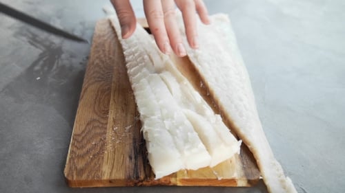 Hands Slicing Raw Fish Fillet on Cutting Board
