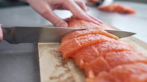 Person Slices Salmon on Cutting Board in Kitchen