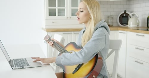 Woman Plays Guitar and Uses Laptop in Kitchen