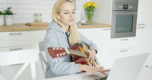Woman Plays Guitar While Using Laptop in Kitchen
