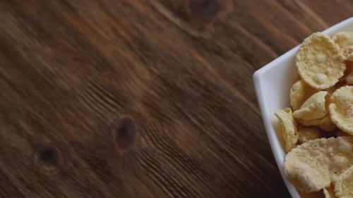 Golden Cornflakes Fill White Bowl on Rustic Wood