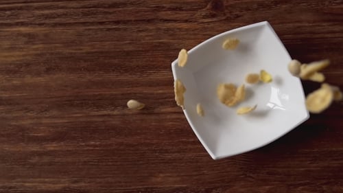 Golden Cornflakes Pouring Into White Bowl on Table