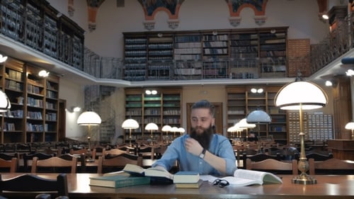 Porträt eines nachdenklichen bärtigen Mannes, der am Schreibtisch der Bibliothek sitzt