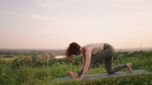 A Young Woman Does Yoga Exercises Standing on the Top of a Forest Mountain Against the Background of