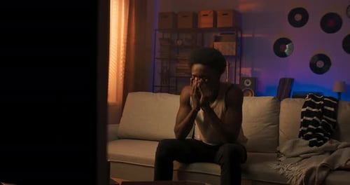 Man Watches TV Looking Sad on Couch