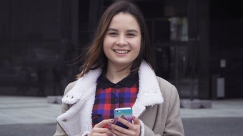 Smiling Woman Holding a Phone in the City