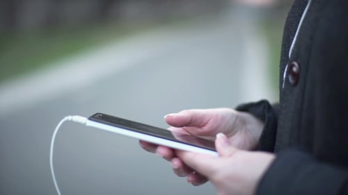 Hands using smart phone with headphones plugged in