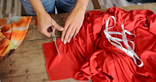 Woman Cutting Red Fabric with Scissors on Table