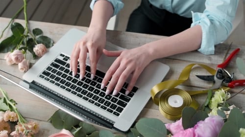 Woman Typing on Laptop Surrounded by Flowers