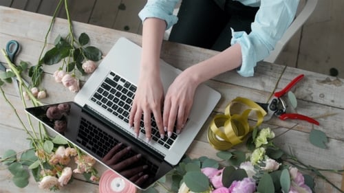 Office Workplace Essentials: Laptop, Paper Notebook, Bouquet of Flowers on the Rustic Wooden Table