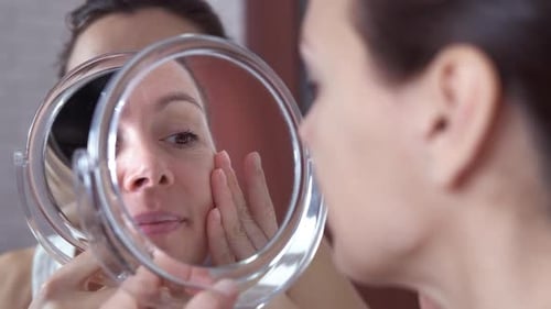 Woman Looks in Mirror Touches Face Close Up